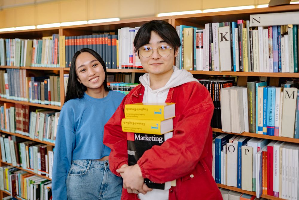 Two students holding books in a library